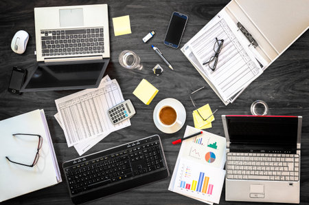 gray office desk at a business meeting with laptops, phones and financial papers, high angle view...