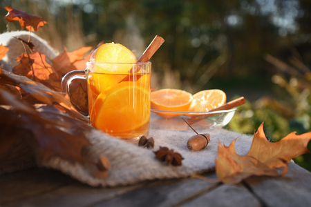 hot tea with orange slices and cinnamon on a wooden garden table with a blanket and autumn leaves, copy space, selected focus, narrow depth of fieldの写真素材
