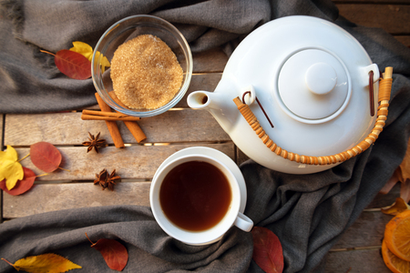 tea cup and a white teapot on a wooden table with spices and some autumn leaves, high angle view from above, selected focusの写真素材