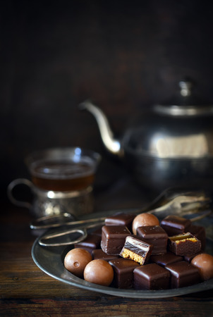 Christmas chocolate sweets on a plate, silver teapot and cup blurry in the dark rusticの写真素材