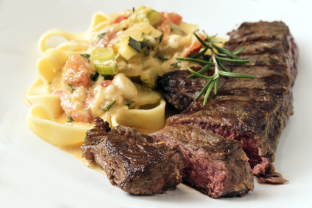 Grilled rump steak with vegetable sauce and pasta on a light gray background, selected focus, narrow depth of fieldの写真素材