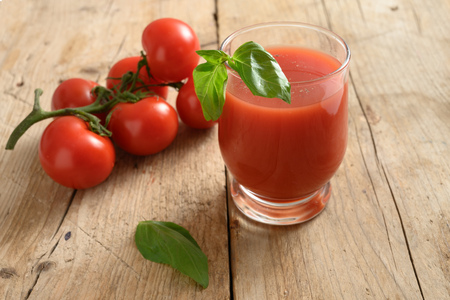 Fresh tomato juice in a drinking glass with basil garnish on a rustic wooden boardの写真素材