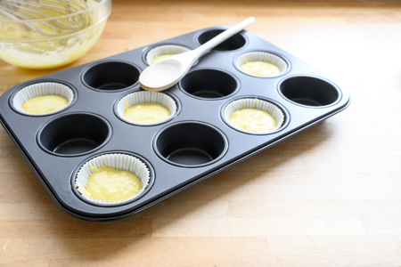 muffin tin, half filled with paper cups and dough for cupcake baking on a wooden kitchen table, copy space, selected focus, narrow depth of fieldの写真素材