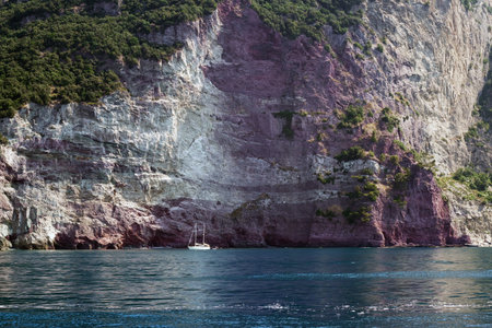 Small sailboat in a bay in front of the rocky cliffs of the Mediterranean seaの写真素材