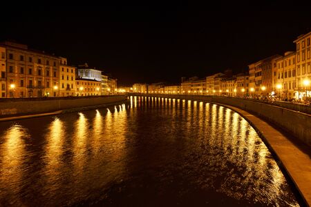 Golden lights on the Arno river shore in the old town of Pisa at night, outdoor summer nightlife with bars used by young people and tourists, copy spaceの写真素材