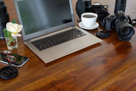 Photographer workplace with laptop, camera, lenses, coffee cup and phone on a wooden table,  copy...