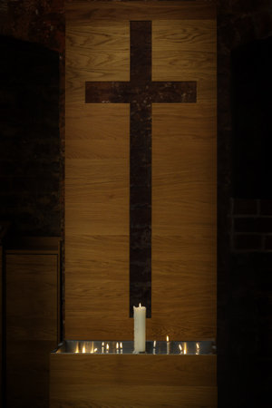 Large and small burning candles in front of a modern simple cross cut out of a wooden plate in the historic St. Georgen churchのeditorial素材