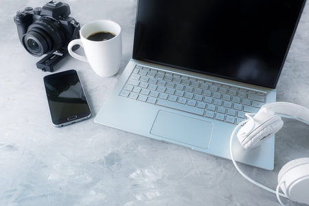 Creative media workplace with laptop, headphones, camera and a coffee cup on a gray