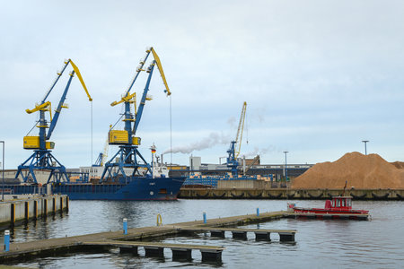 WISMAR, GERMANY, FEBRUARY 2, 2020: Crane boat, fire brigade ship and a wood processing factory  in the timber port of Wismar in Mecklenburg-Western Pomerania, cloudy sky with copy spaceのeditorial素材