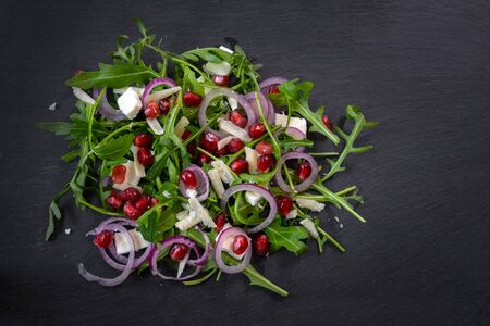Arugula or rocket salad with pomegranate seeds, red onions and parmesan on a dark slate plateの写真素材