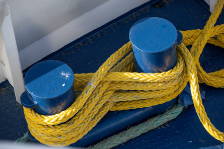 yellow ship rope tied around blue mooring bollards on a metal boat deck
