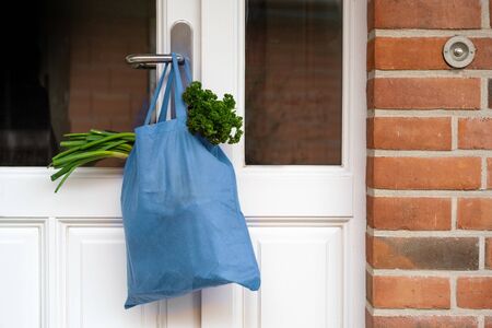 Blue shopping bag with fresh vegetables and goods was hanged on the front doorの写真素材