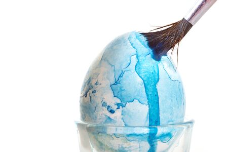 Easter egg painting with a brush and blue watercolor and a brush, isolated on a whiteの写真素材