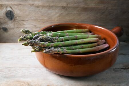 Organic green asparagus (Asparagus officinalis) fresh from the market in a brown ceramic bowl on a rustic wooden board, selected focus, narrow depth of fieldの写真素材