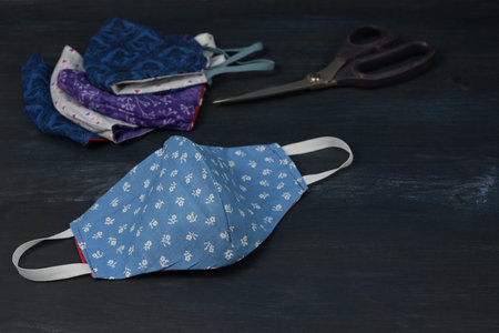 Homemade community face masks sewn from blue patterned cotton on dark painted wood