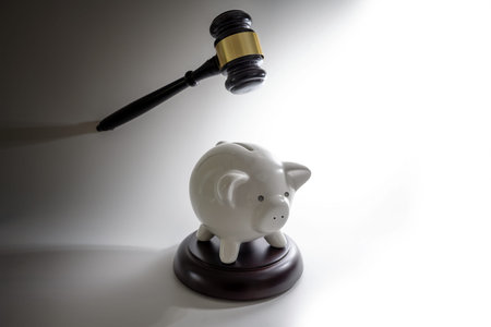 Unsuspecting piggy bank under the judge's gavel, coming from the dark, economy concept, gray...