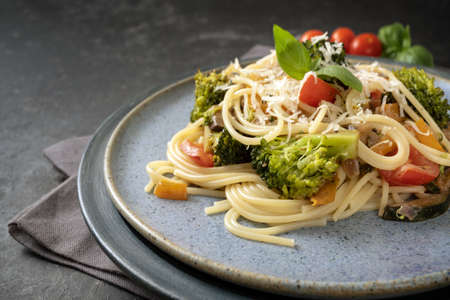 Spaghetti with vegetables like broccoli, tomatoes and bell pepper, healthy vegetarian pasta meal on a blue plate and a gray rustic background, selected focus, narrow depth of fieldの写真素材