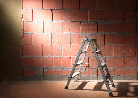Step ladder in front of a brick wall from Porotherm style blocks partly plastered with clay in a construction site of a new building, copy spaceの写真素材
