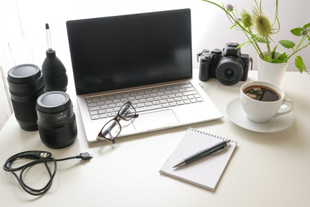 Workplace of a photographer, white office desk with laptop, camera, equipment, notepad and a cup of...