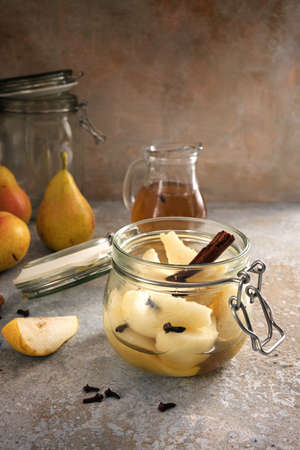 Glass jar with canned pears flavored with cinnamon and cloves and some fresh fruits on a rustic vintage stone background, copy space, selected focus, narrow depth of fieldの写真素材