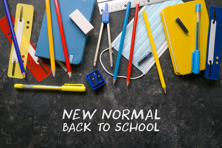 Stationery school supplies and a medical protection face mask against coronavirus and covid 19 infection on a dark background, text New Normal Back to School, high angle view from aboveの写真素材