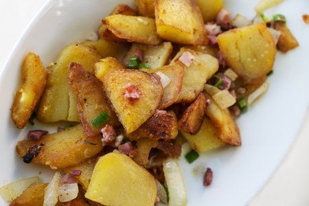 Crispy golden fried potatoes with onions and bacon served on a white plate, high angle view from...