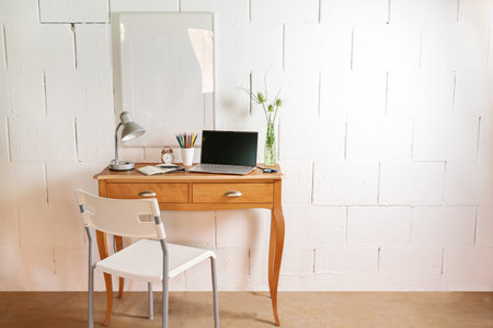 Small wooden table and chair as a tiny place for a home office with laptop, desk lamp and tools...