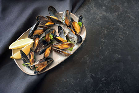 Fresh blue mussels served with lemon and parsley on a plate, dark slate background with large copy space, high angle view from above, selected focus, narrow depth of fieldの写真素材