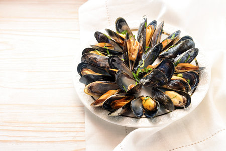 Fresh blue mussels with herbs served on a white plate on a bright wooden table, copy space, selected...