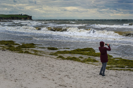 Woman takes photos of wild waves in storm and onshore wind at the beach of Boltenhagen at the Baltic...