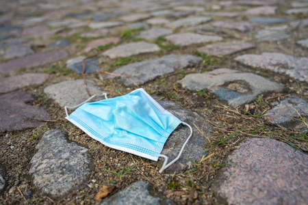 Thrown away surgical face mask against infection with coronavirus and covid-19 on cobblestones, copy space, selected focus, very narrow depth of fieldの写真素材
