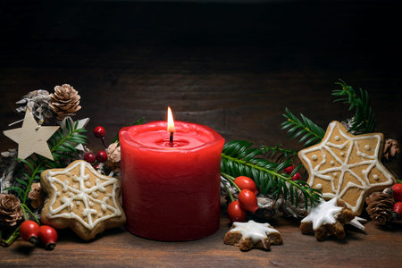 Christmas decoration with a red burning candle, gingerbread cookies, rose hips, branches and cones...