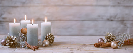 Four burning candles and Christmas decoration like cones, cinnamon and baubles against a rustic...