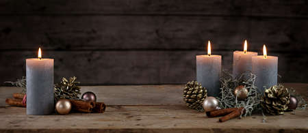 Burning candles and Christmas decoration like cones, baubles and cinnamon sticks on a rustic wooden table against a dark background, panoramic format, copy space, selected focus, narrow depth of fieldの写真素材