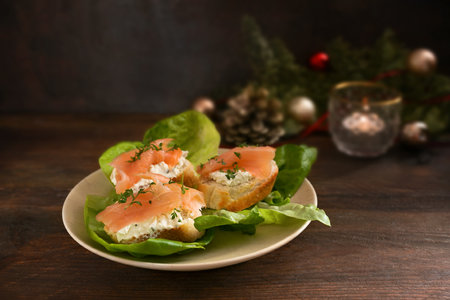 Festive canapes from baguette bread with salmon and cream cheese on green lettuce on a dark rustic wooden table with Christmas decorations, copy space, selected focus, narrow depth of fieldの写真素材