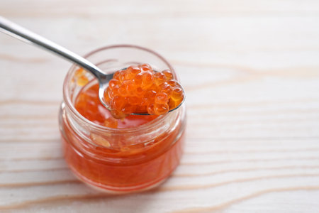 Red caviar on a spoon and in a glass on a white painted wooden table, festive seafood snack for holidays, copy space, selected focus, narrow depth of fieldの写真素材