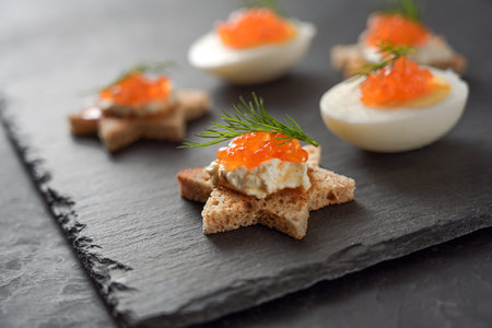 Star shaped canapes and halved eggs with red caviar and dill garnish on a dark slate plate for a festive holiday buffet, copy space, selected focus, narrow depth of fieldの写真素材