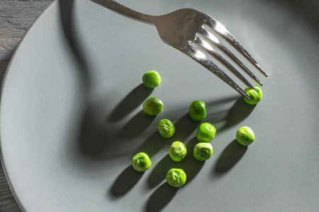 Some green peas and a fork with shadows on a gray plate, meager diet meal after the resolution to slim down, copy space, selected focusの写真素材