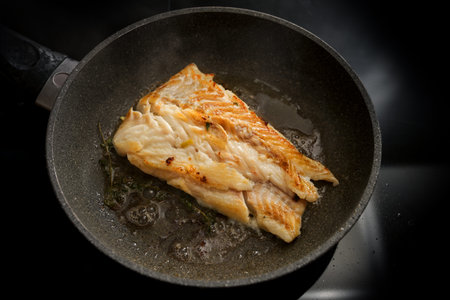 Cod fish fillet sautÃ©ed in butter in a frying pan on the stove, selected focus, narrow depth of...