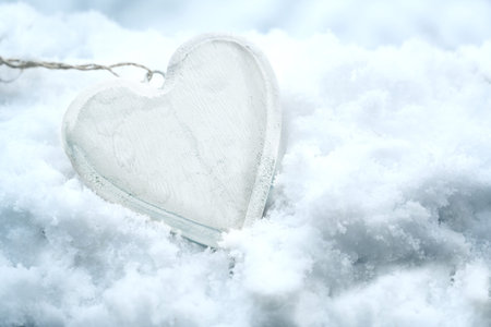 White painted wooden heart shape lying in the snow, seasonal winter love symbol for valentines day,...