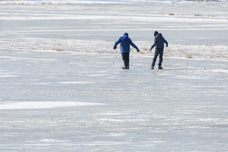 Two boys on a frozen lake frightened by a melted puddle in the weak ice, dangerous recreational fun in thawing weather, copy space, selected focusの写真素材