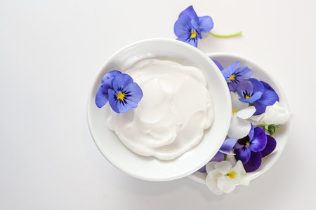 Natural cosmetic ointment and viola or violet flowers in white bowls on a light gray background, copy space, high angle view from above, selected focus, narrow depth of fieldの写真素材