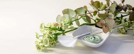 Cosmetic moisturizer mask in a bowl with a brush and green flower branches on a light background, panoramic format, copy space, selected focus, narrow depth of fieldの写真素材