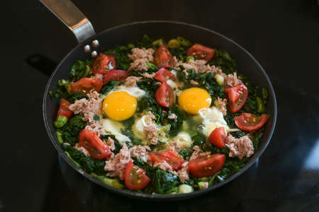 Spicy spinach with tomato, tuna and egg in a pan on the black stove, cooking a healthy low carb diet meal, selected focus, narrow depth of fieldの写真素材