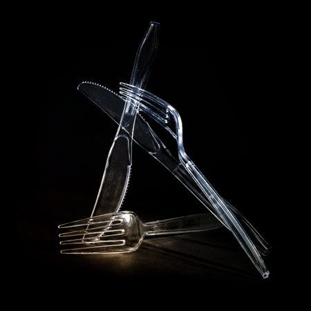 Transparent plastic cutlery, knives and forks against a black background, disposable tableware will...
