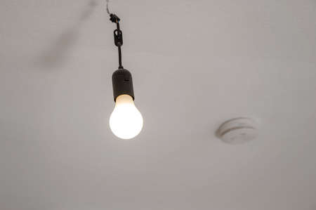 Dusty light bulb without lampshade hanging switched on from the ceiling in an empty apartmentの写真素材