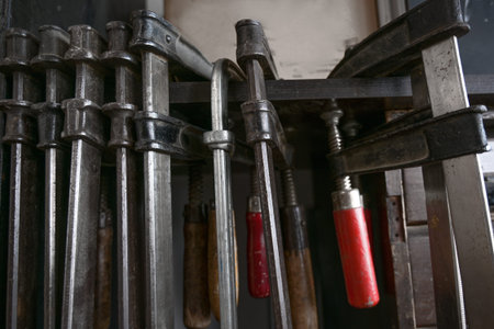 Screw clamps hanging in a row in the workshop of a craftsman, copy space, selected focus, narrow...