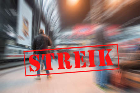 Man waiting for the train on a platform in the big city railway station and banner with German text Streik (meaning strike), blurred crowd background with zoom effect, copy spaceの写真素材