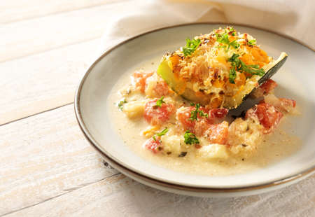 Slice of baked zucchini stuffed with vegetables and parmesan with a sauce from tomato and feta cheese on a plate and a light rustic wooden table, copy space, selected focus, narrow depth of fieldの写真素材