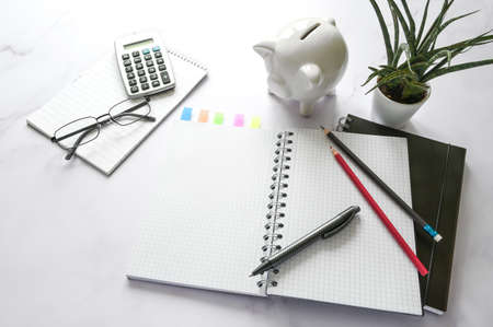 Office desk with a blank notebook, piggy bank, calculator and stationary supplies on a marble surface, copy space, selected focus, narrow depth of fieldの写真素材